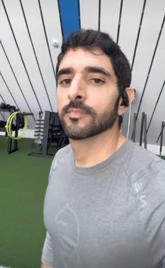 a man standing in front of a gym with equipment on the wall and green flooring