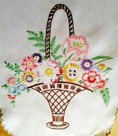 a basket filled with flowers on top of a white cloth covered table next to a wooden surface