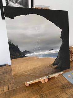 an easel sitting on top of a wooden floor next to a painting with a lightning in the sky