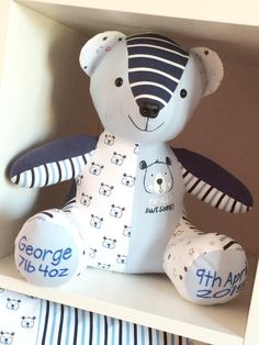 a teddy bear sitting on top of a white book shelf with blue and white striped sheets