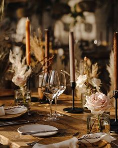 a wooden table topped with plates and glasses filled with flowers, candles and napkins