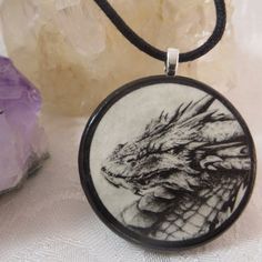 a necklace with a drawing of a dragon on it next to some rocks and crystals