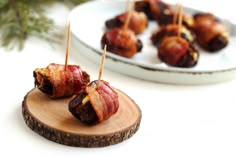 bacon wrapped dates sitting on a wooden board next to a white plate with pine branches