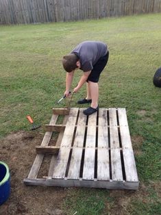 a man is bending over to pick up something on top of some pallets in the yard