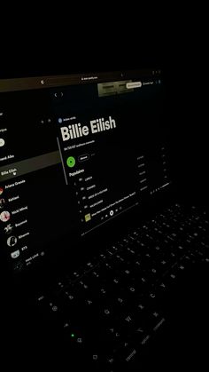 a laptop computer sitting on top of a black desk with the words bille eliish written on it