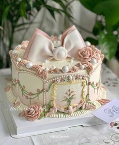 a decorated cake with pink flowers and bows on it's top is sitting on a table