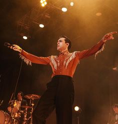 a man standing on top of a stage holding his arms out to the side while wearing a red shirt and black pants