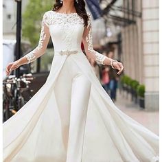 a woman is walking down the street wearing a long white dress with sheer sleeves and lace detailing