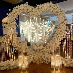 a wedding arch with candles and flowers in the shape of a heart that says will you marry me?