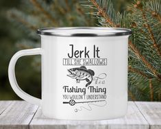 a white enamel mug with fishing sayings on the side and pine tree in the background