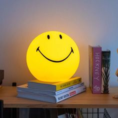 a yellow smiley face lamp sitting on top of a table next to books and a teddy bear