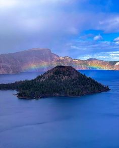 an island with a rainbow in the sky above it and water below that is surrounded by mountains