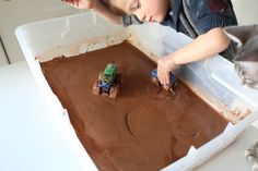 a boy is playing with his toy trucks in the chocolate mud bath that he made for his cat