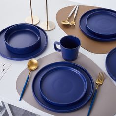 a table set with blue plates, silverware and gold utensils