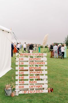 DIY Order Of The Day pallet painted white with orange writing and floral decor Wedding Sign Post, Signage At Wedding, Pallets At Weddings, Outdoor Event Decor Diy Ideas, Diy Outdoor Wedding Ideas, Palette Wedding Sign, Creative Wedding Signage, Diy Painted Wedding Signs, Wedding Direction Sign