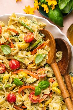 a white plate topped with pasta and veggies covered in sauce next to wooden spoons