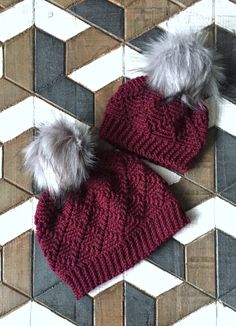 two knitted hats with fur pom poms on top of a tiled floor