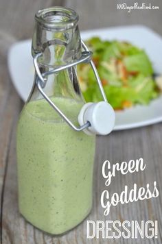 a bottle filled with green goddess dressing next to a salad on a white plate and wooden table