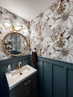 a bathroom with blue walls and floral wallpaper on the walls, along with a round mirror