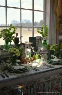 the table is set with dishes and flowers in vases on it, near a window