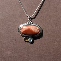 "Superb Lake Superior Agate Pendant set in .925 Sterling Silver and features a Citrine and Blue Moonstone below. Small amount of antique finish around silver decorations. Solid silver back.  Chain not included  Piece measures about 1\" x 1.5\" Our reviews will tell you, If you like it here, you'll LOVE it in person! GIVE IT A TRY! If not completely satisfied with your order, contact me right away and return the item within 7 days. FIND WHAT YOU LOVE: Use the \"Sections\" box (or \"Items\" list area) to see the categories. Or use the \"Search Items\" bar to search FUN terms like: eyes, tubes, water level, moon, Easter Island, double, gecko, heart and sale!  Instagram: www.instagram.com/agatejewelrybylarry Facebook fb.me/agatejewelrybylarry Custom work not available at this time. pendant cha Spiritual Silver Gemstone With Oval Pendant, Spiritual Silver Oval Pendant Gemstone, Oval Multi-stone Cabochons For Gifts, Silver Carnelian Cabochon Necklace, Silver Carnelian Jewelry For Anniversary, Antique Beads, Gems, And Cabochons As Gifts, Carnelian Gemstones As Gifts, Spiritual Multi-stone Oval Gemstones, Oval Silver Natural Gemstones