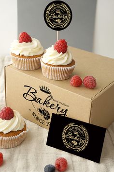 three cupcakes with white frosting and raspberries in front of a box