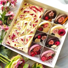 a box filled with lots of different types of cakes and flowers on top of a table