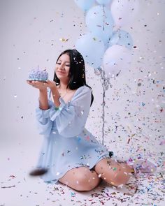 a woman sitting on the floor with a cake and balloons in front of her as confetti falls around her