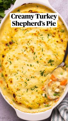 a white casserole dish with cheese and vegetables in it next to a green leafy garnish