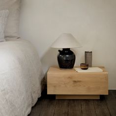 a night stand with a lamp on it next to a bed