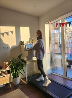 a woman standing on a treadmill in front of a window with bunting flags