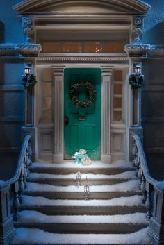 a green door with a wreath on it in front of snow covered steps and stairs