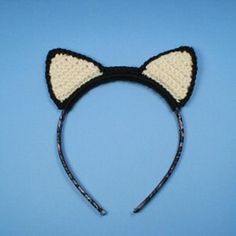 a crocheted cat ears headband with black and white yarn on top, against a blue background