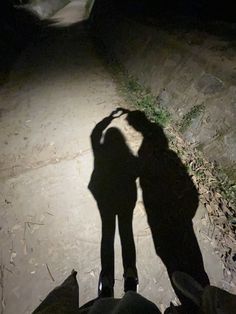 the shadow of two people standing in front of a stone wall at night with their hands on their head