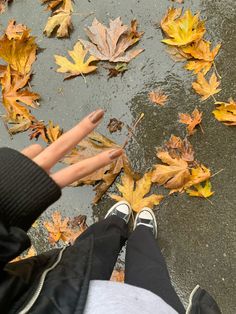 a person is standing on the ground with their feet in the water and leaves all around them