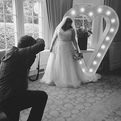 a man taking a photo of a bride in front of a heart shaped light up mirror