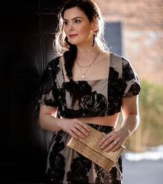 a woman standing in front of a black door holding a brown purse and looking at the camera