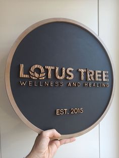 a person holding up a plaque that says lotus tree, wellness and healthing