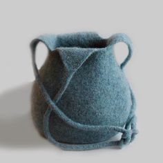 a blue felted vase with a handle on a white table next to a pen