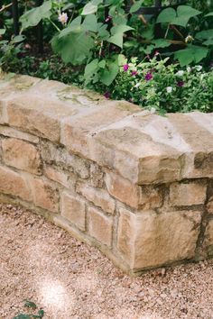 a stone wall in the middle of a garden with flowers growing on it's sides