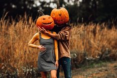 a man and woman hugging each other with pumpkins on their heads in the middle of a field