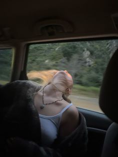 a woman sitting in the back seat of a car with her hair blowing in the wind