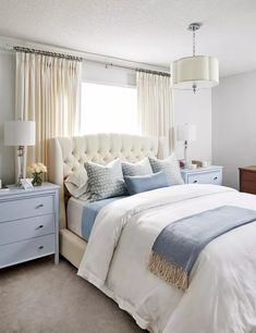 a bedroom with white and blue bedding, two nightstands and a large window