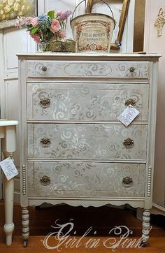 a white dresser with ornate designs on the top and bottom drawers, along with a basket full of flowers