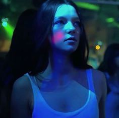 a young woman standing in front of a crowd at night with blue light on her face