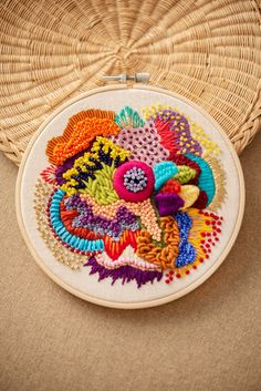 a close up of a colorful embroidery on a piece of cloth with a basket in the background