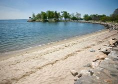 a sandy beach next to the ocean with trees in the distance and rocks on the shore