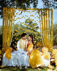 a man and woman sitting on top of a bed under a yellow canopy covered in flowers