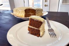 a slice of carrot cake on a white plate with a fork next to the rest of the cake