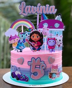 a pink and blue birthday cake with cartoon characters on the top, sitting on a table